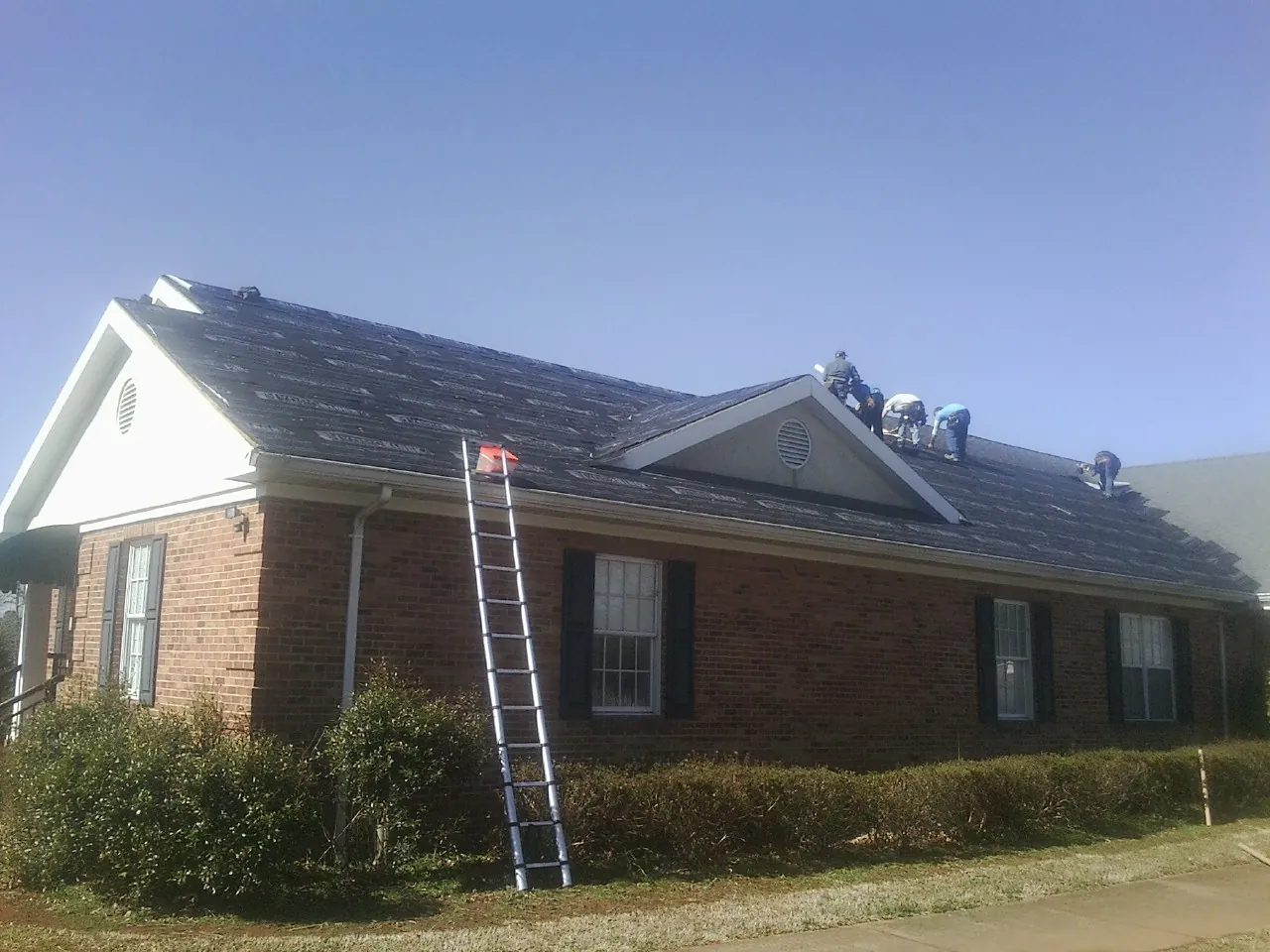 Crew tearing shingles off a brick ranch roof with a ladder set — Emergency Roof Repair work by our crew in Freedom